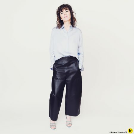 Frau in hellblauer Seidenbluse mit weiter, dunkelblauer Lederhose und Pailletten-Sandalen.