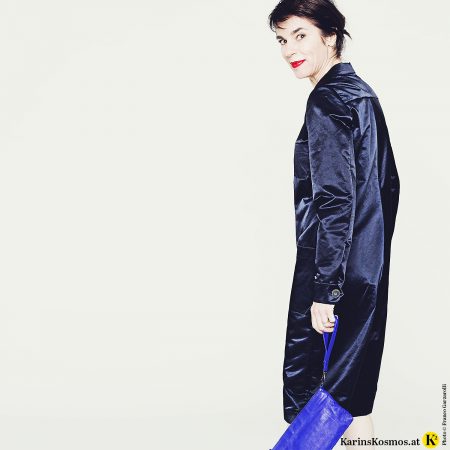 Frau mit rotem Lippenstift und in mitternachtsblauem Satin-Overall mit blauer Clutch.