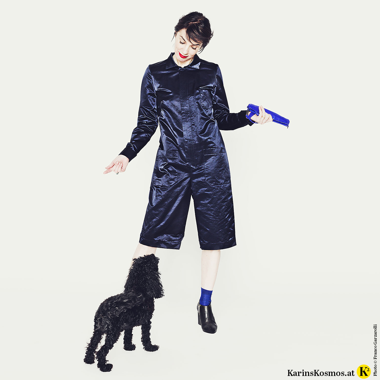 Frau stehend in Overall mit Toypudel Trudy vor ihr stehend.
