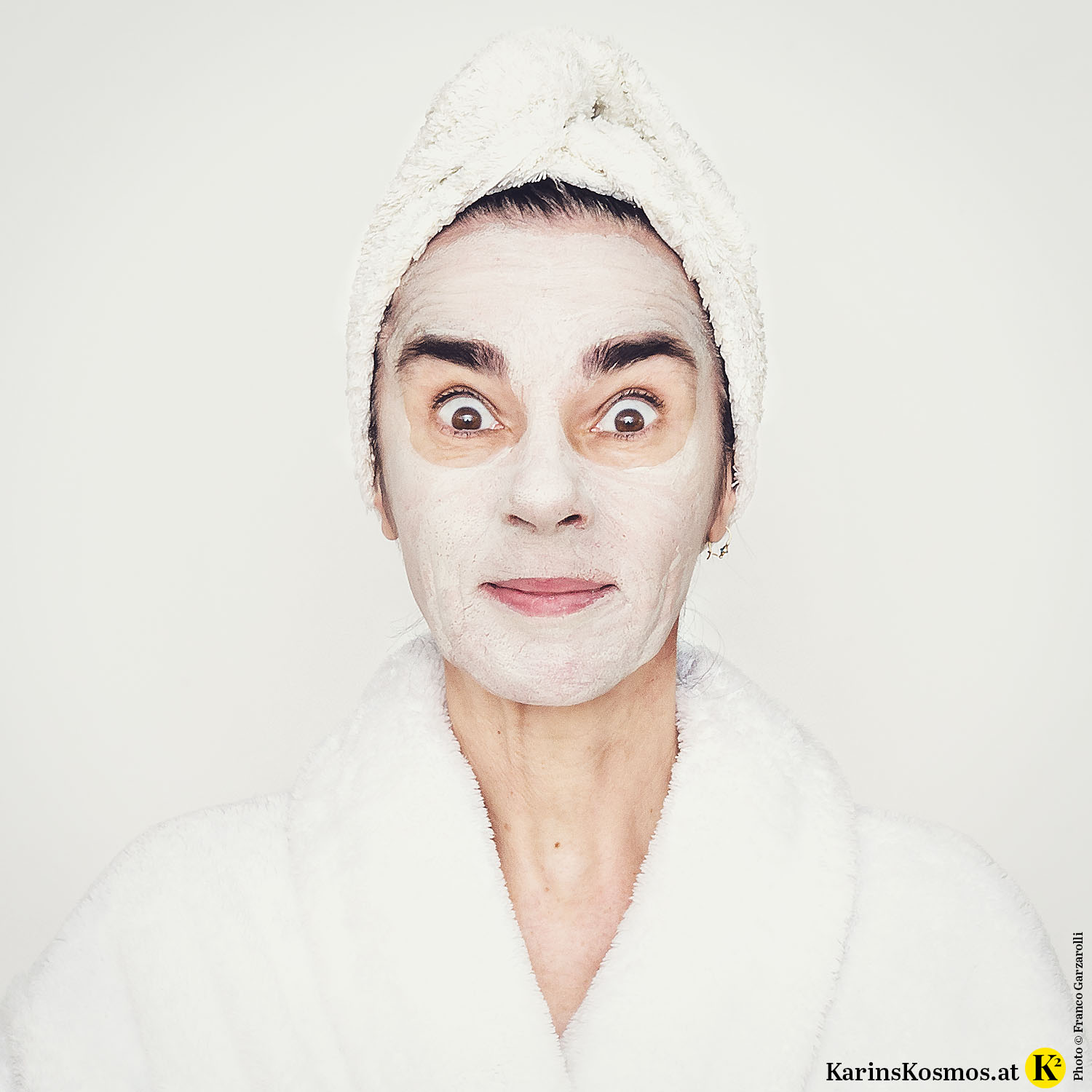 Frau mit Handtuch am Kopf und Bademantel mit Maske im Gesicht.