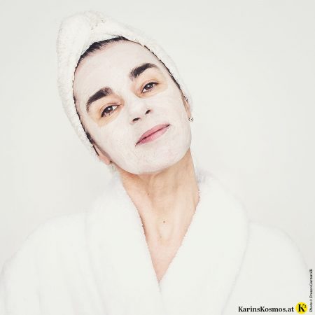 Frau mit Bademantel und Handtuch am Kopf und Maske im Gesicht.