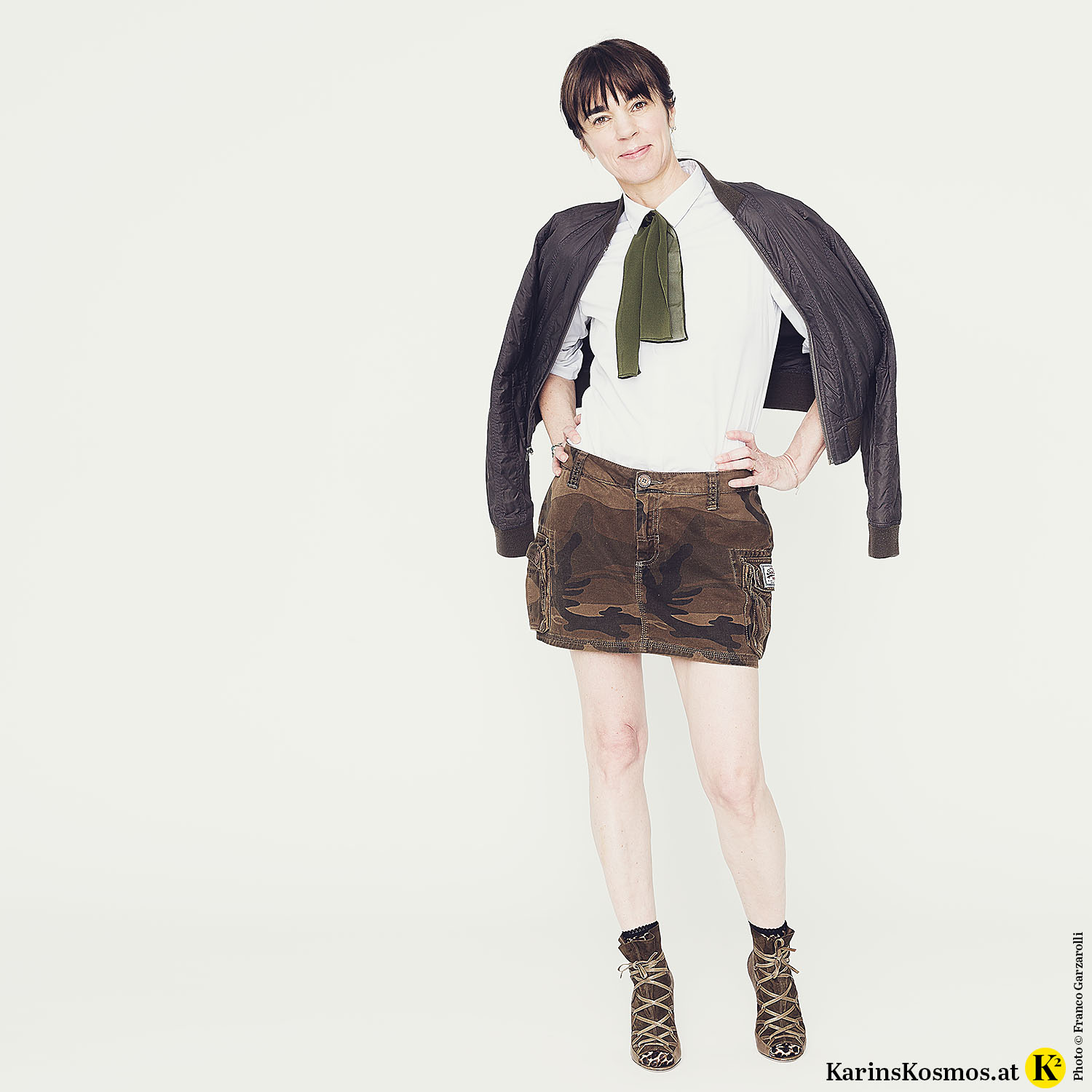 Frau in Minirock mit High-Heels, weißer Bluse und Bomberjacke.