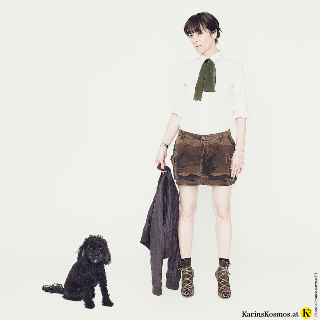 Frau in einem Minirock plus High-Heels und daneben ein sitzender Toypudel.