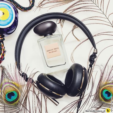 Foto mit einem Parfumflakon, Kopfhörer, Pfauenfedern und einem griechischen Auge.