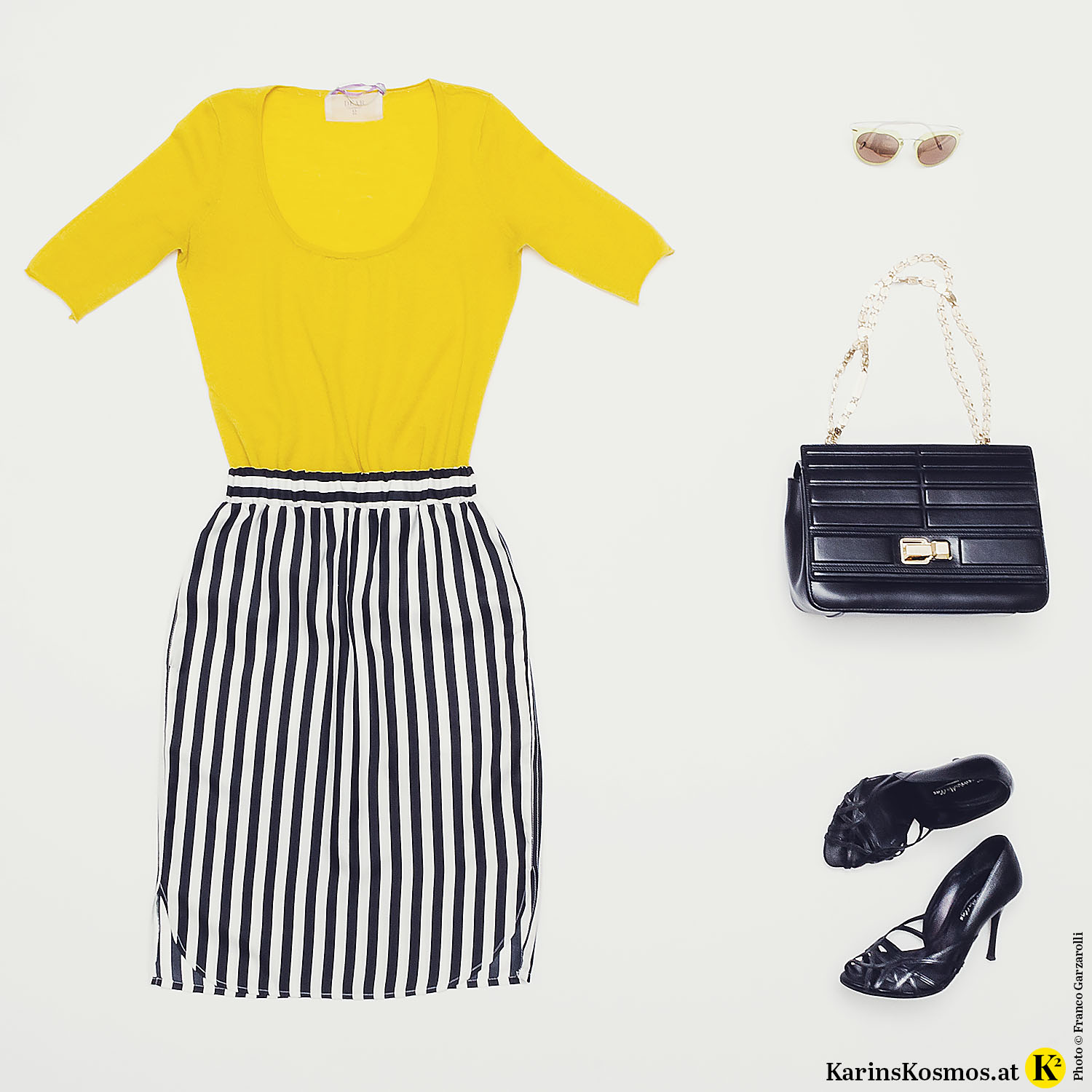 Produktfoto mit gelbem Kaschmir-Shirt, Seidenrock mit schwarz/weißen Streifen, Sonnenbrille, Ledertasche mit goldenem Henkel und schwarzen Pumps.