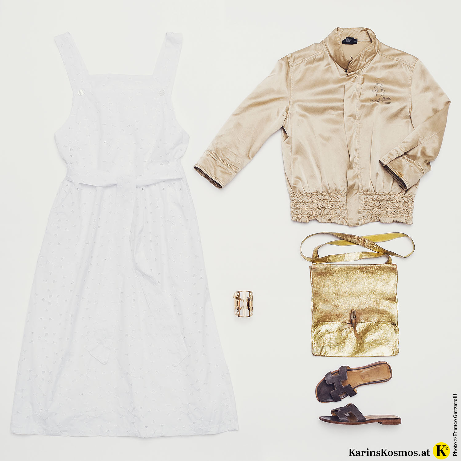 Produktfoto mit weißem Kleid, beiger Bomberjacke, goldenem Armreif und Tasche und braunen Leder-Slippers.