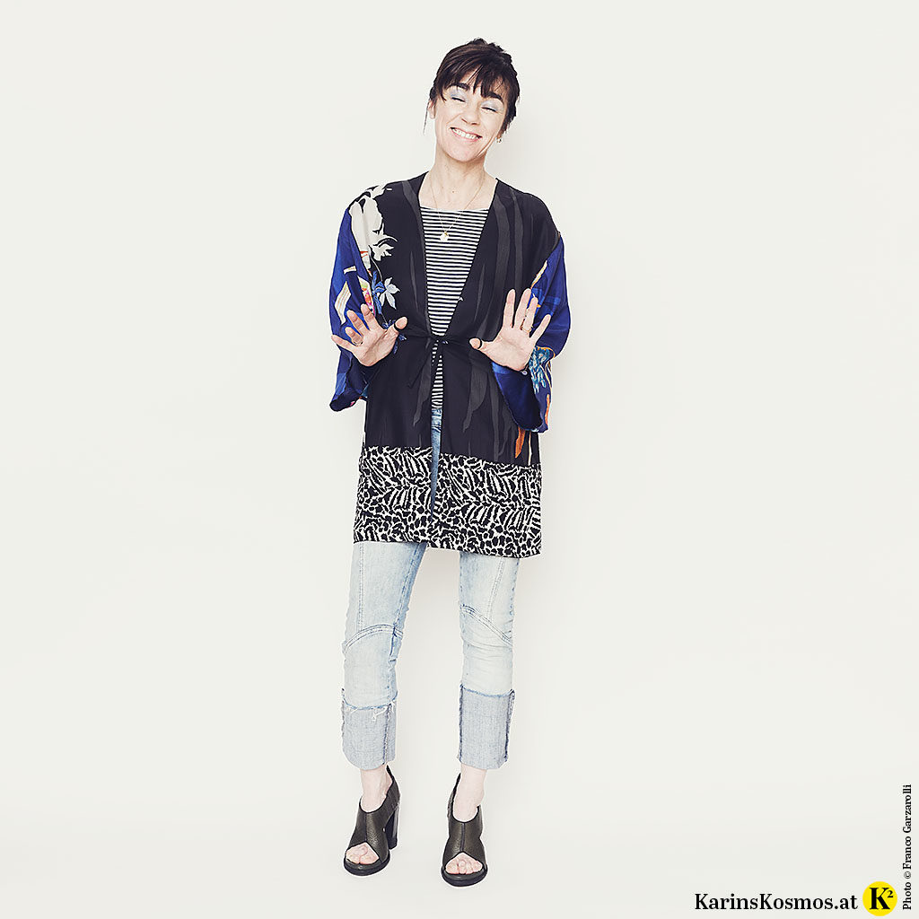 Frau mit einem Kimono, Streifen-Shirt, Jeans und Sandalen.