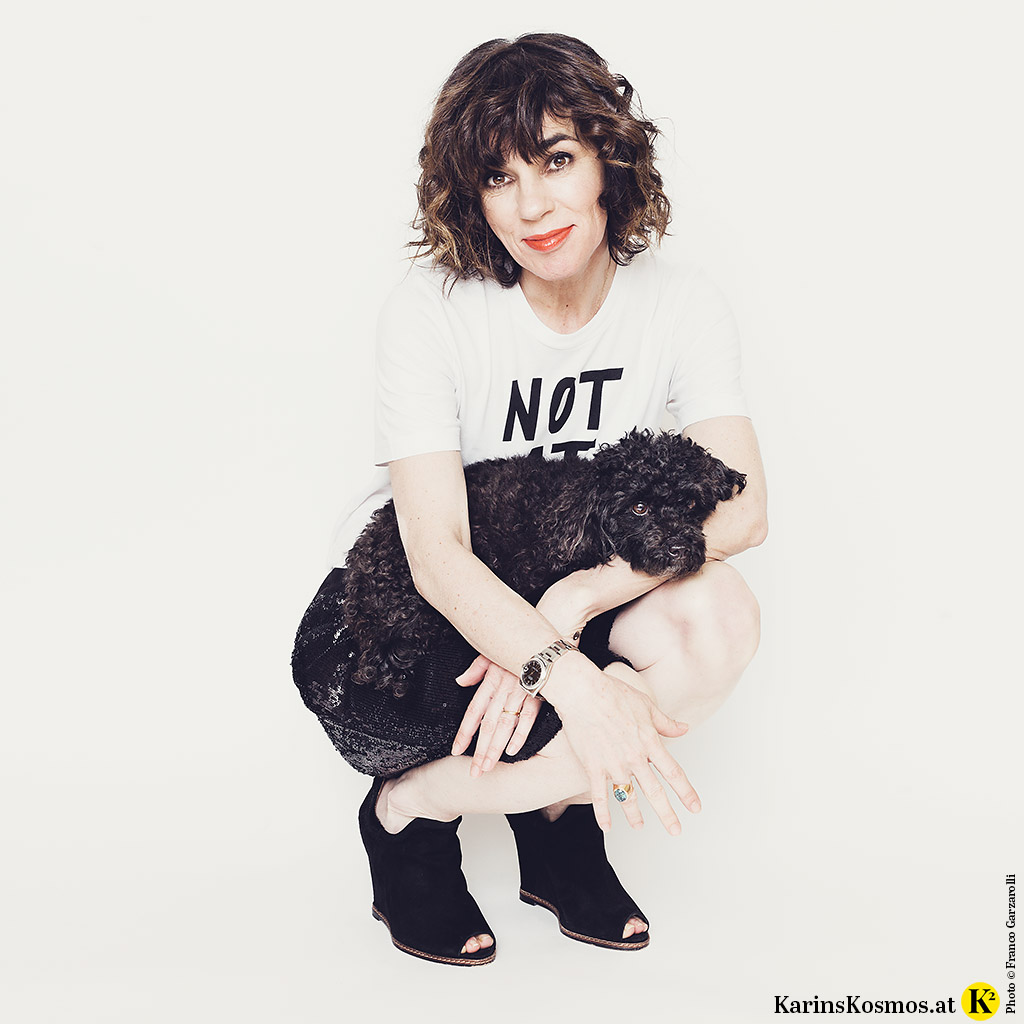 Frau in Pailletten-Shorts und Logo-Shirt mit einem schwarzen Toypudel.