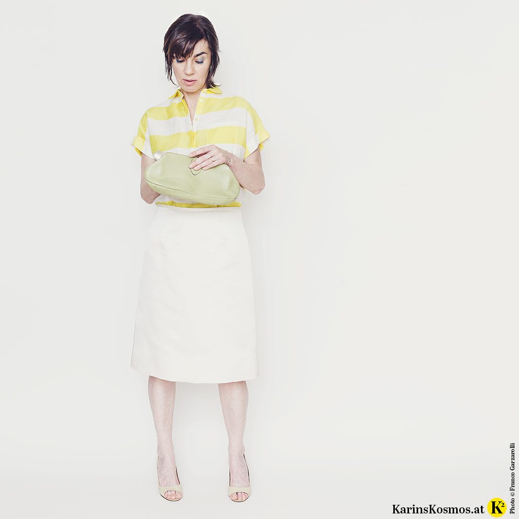 Frau mit Satinrock in weiß, dazu Leinenbluse, Heels und Clutch.