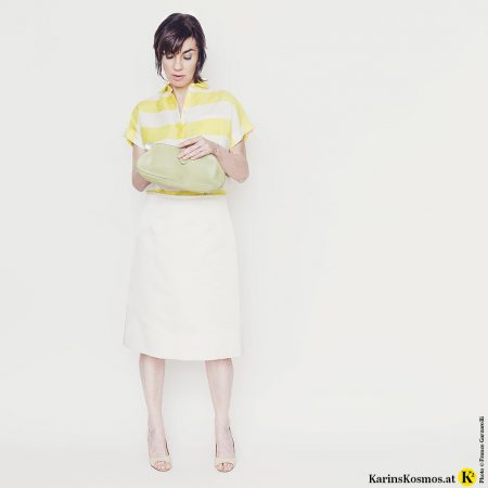 Frau mit Satinrock in weiß, dazu Leinenbluse, Heels und Clutch.