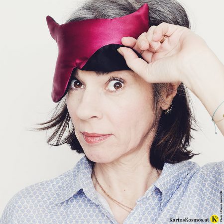 Frau mit einer Schlafmaske aus Seide um wach dreinblickenden Augen.