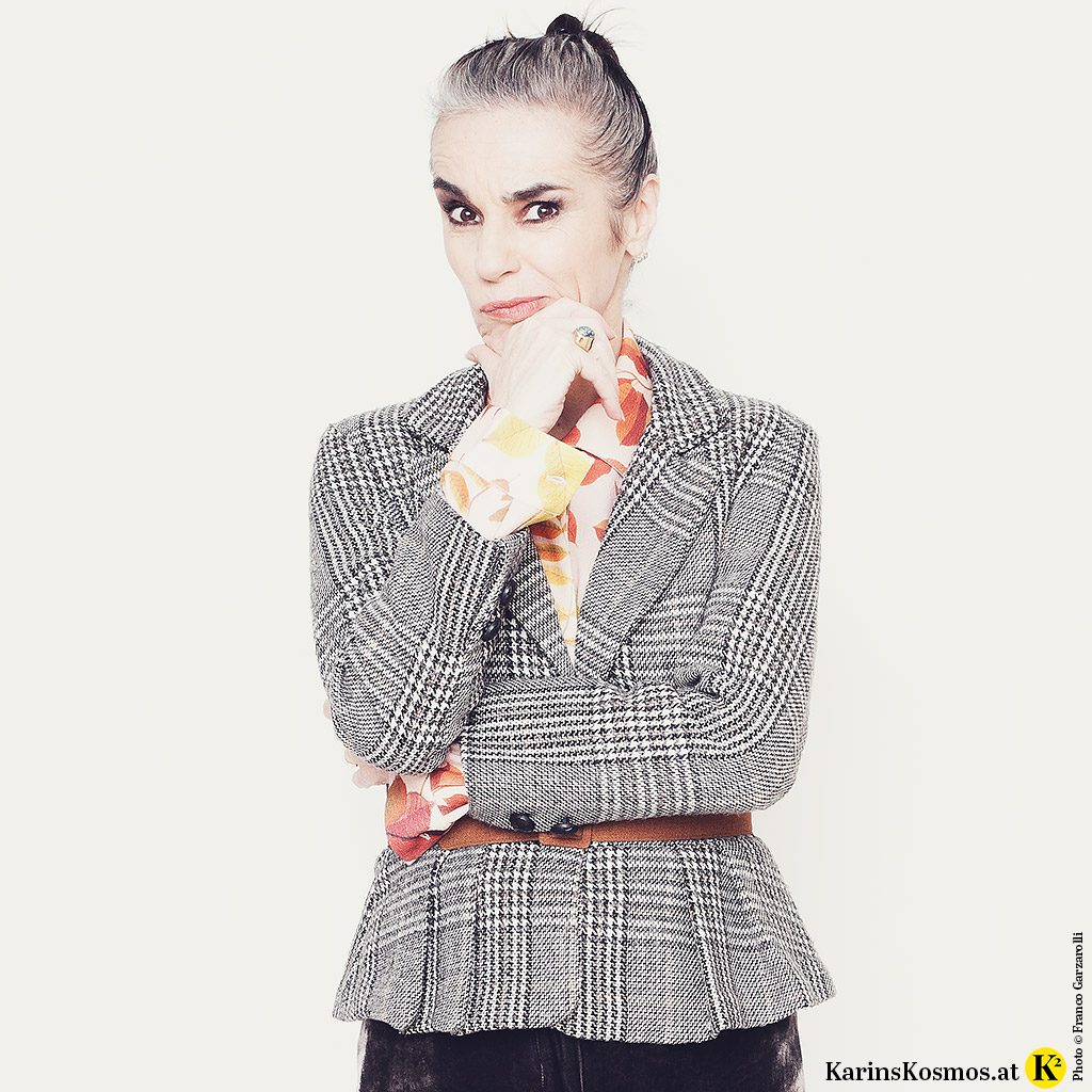 Frau in einem Karo-Blazer zu einer bunten Bluse mit Blätter-Print.