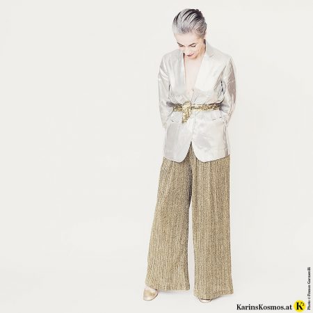 Frau in Metallic-Mode in Form eines Blazers in Hochglanzsilber und Goldhose.