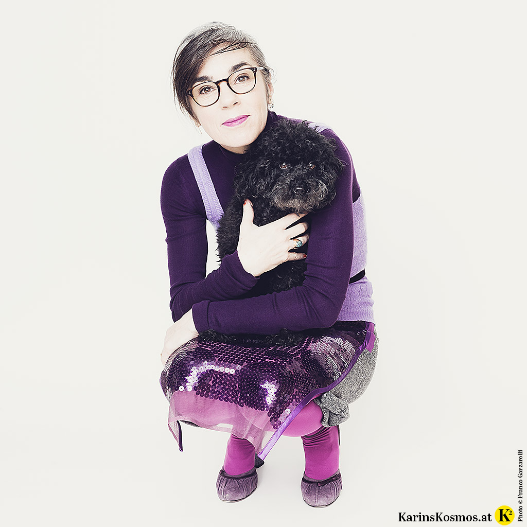 Frau in einem Outfit in Ultraviolett mit kleinem Toypudel am Arm.