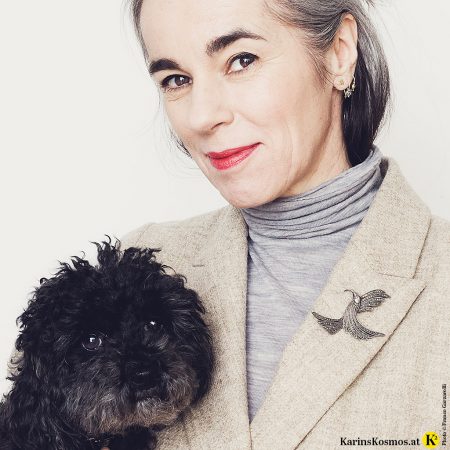 Frau mit einem Blazer und Vintage-Brosche am Revers. Am Arm trägt sie einen schwarzen Pudel.