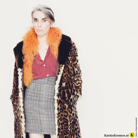 Frau in einer getupften Seidenbluse zu kariertem Rock, Mantel in Leoprint und orangen Fellschal – kurzum im wilden Mustermix!